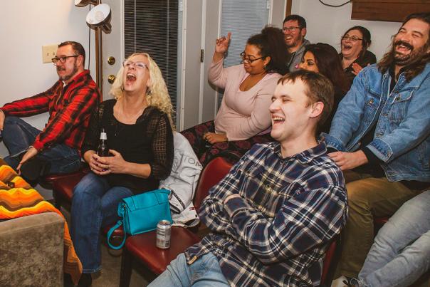 Seated audience in small, intimate space with laughing and smiling faces during a Lampshade Media comedy performance