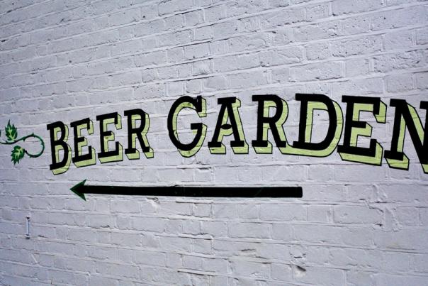 A white brick wall with a painted sign in black and green 'beer garden' with an arrow pointed left