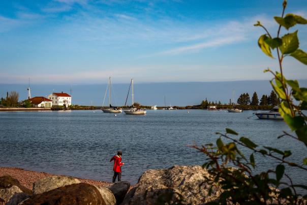 A child plays on the beach in Harbor Park with sailboats in the background