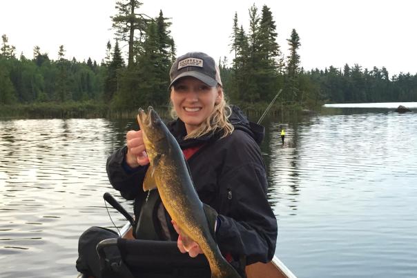 A woman holding a walleye in a canoe.