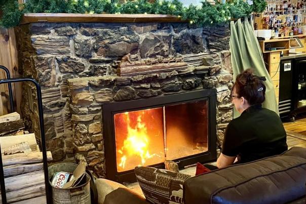 Woman sitting in front of a roaring fire in a lodge fireplace.