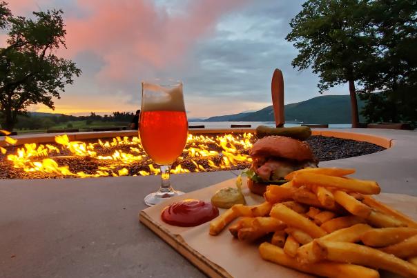 An image of a hamburger and fries with a beer in front of the firebar at the Otesaga