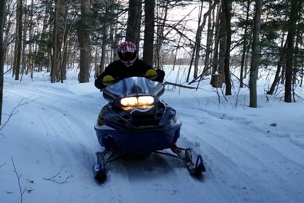 an image of a snowmobile and rider on a snowy trail in the woods