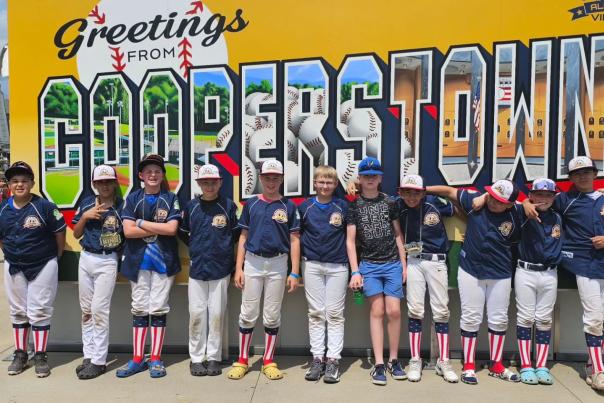 a youth baseball team lined up in front of a yellow sign that says greetings from cooperstown