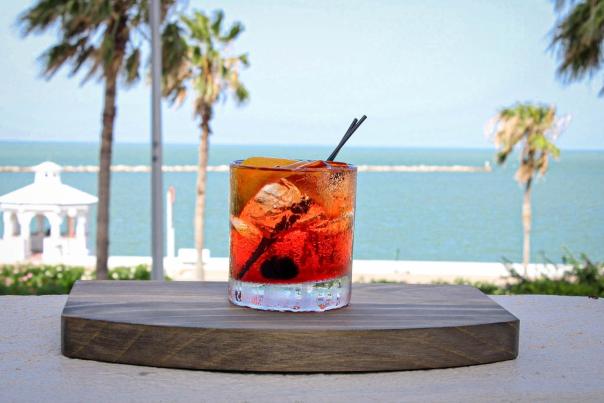 Bright red-orange cocktail with orange slice by the sea and palm trees