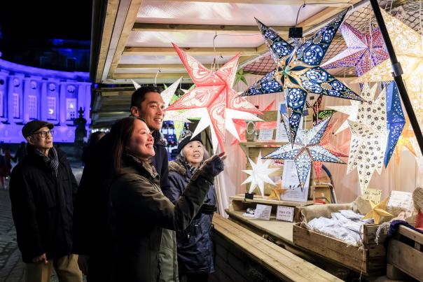 A group of people look at star lanterns in a wooden chalet at Blenheim Palace Chrsitmas Market