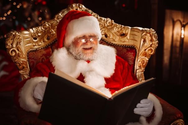 Santa sits in an ornate chair reading a book