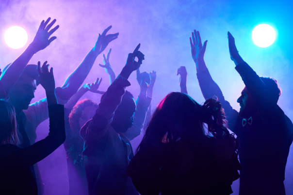 The picture shows a group of men and women dancing in a nightclub with their arms in the air.
