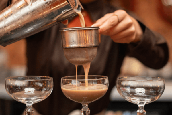 Image shows cocktails being poured at a bar.