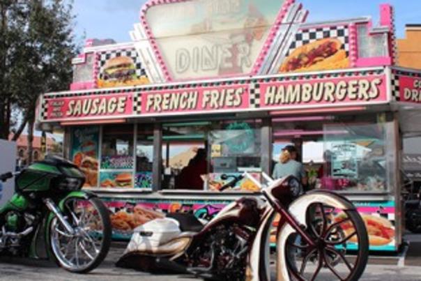 Custom motorcycle stretched out in front of a colorful hamburger stand.