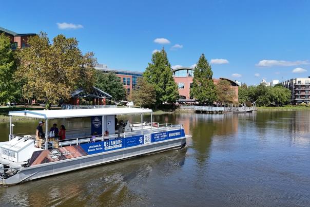 A Delaware Cruise moving along the water beside Riverfront Wilmington on a sunny day.