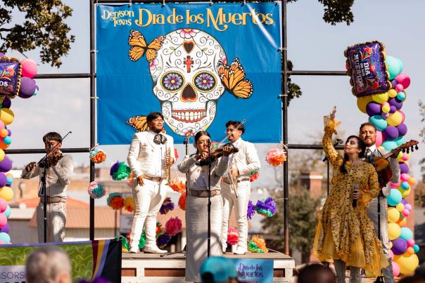 Mariachi Performers and singer on stage in front of Dia de los Muertos banner for the annual event