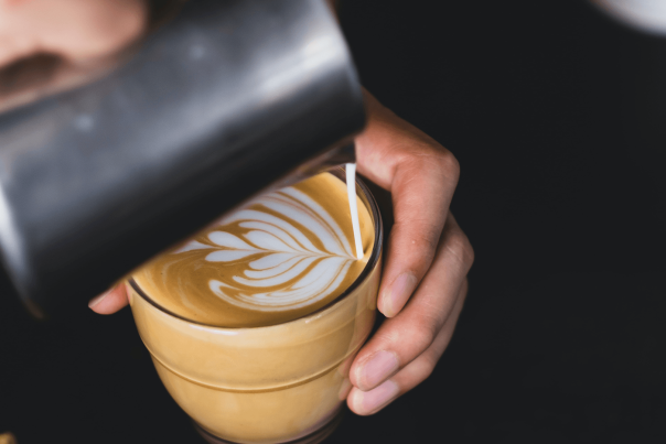 A barista is pouring latte art into a glass cup.