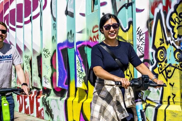 A couple on scooters riding by a street mural in Denver's River North Art District.