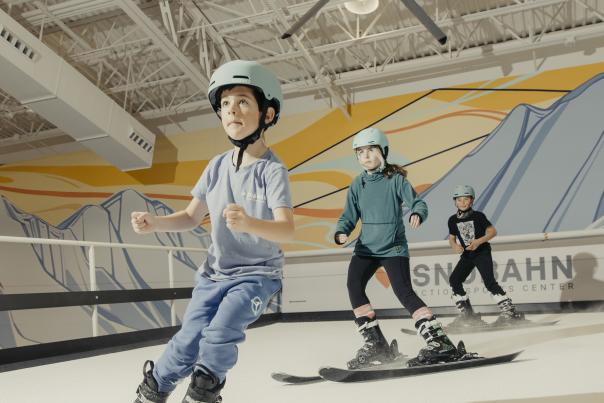 Three kids learning to ski on Snobahn's indoor slope simulator.