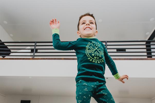 A child in pajamas jumping for joy on a hotel bed at The Maven Hotel.