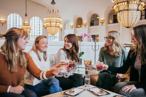 Five women at a table holding up their drinks in Cooper Lounge at Denver Union Station