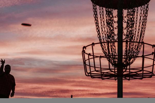 A person tosses a disc into the net at a disc golf course at sunset