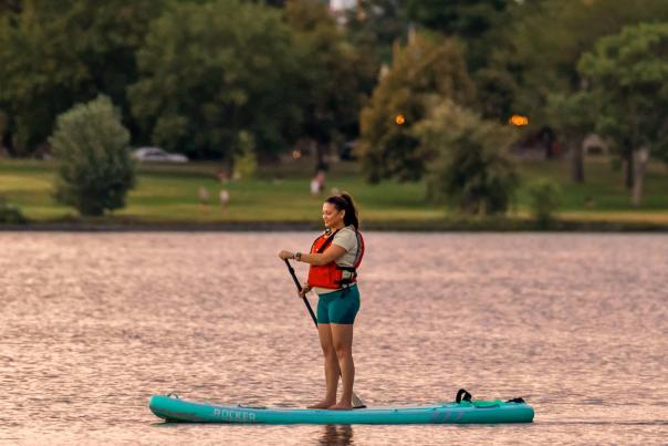 A person wearing a life preserver paddles on Sloan's Lake at sunset