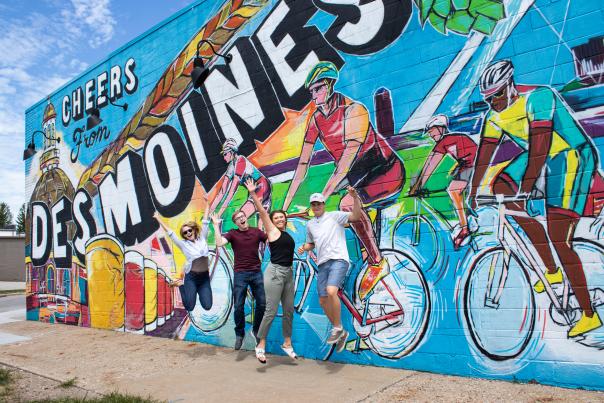 Friends jump in joy in front of the "Cheers from Des Moines" mural in downtown Des Moines.