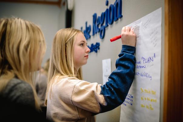 A young adult writing on a jumbo sticky note.