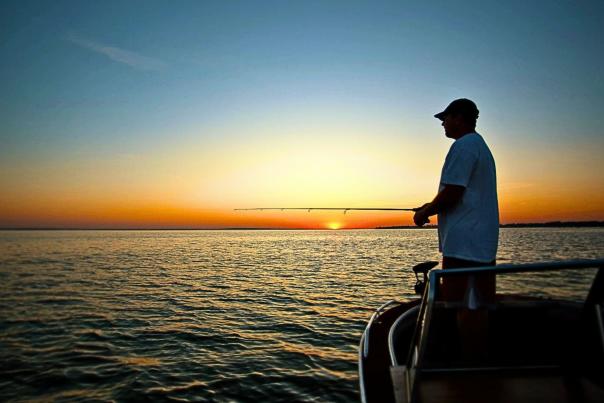 Man fishing in a boat on Devils Lake, ND, with sunset on the horizon.