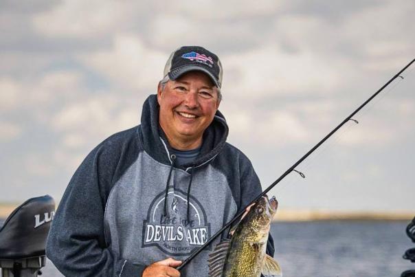 Johnnie Candle is on a boat on Devils Lake, North Dakota, holding up a large walleye he just caught.
