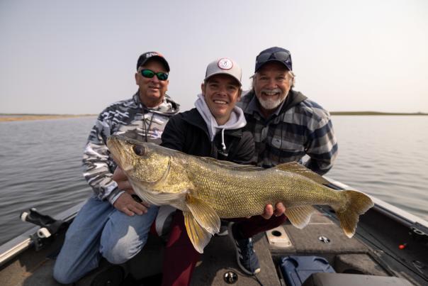 three men holding a large walleye in a boat