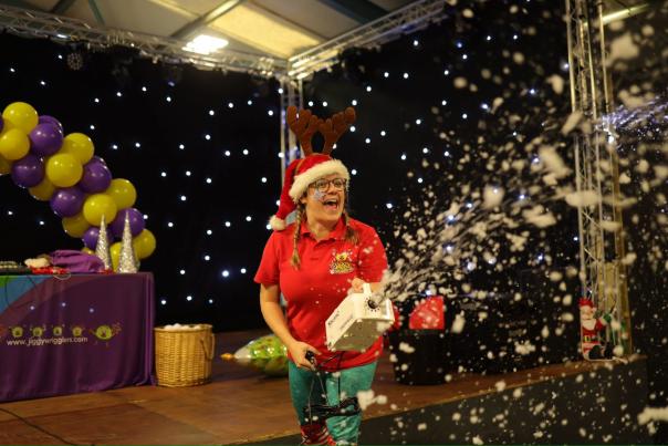 A worker at the big sheep wearing a christmas hat and antlers spraying fake snow at a christmas party
