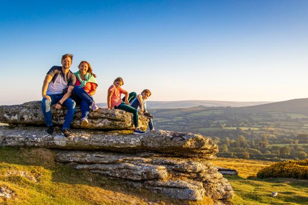 a family of two adults and two children sitting on a flat rock in Dartmoor with spectacular view behind them