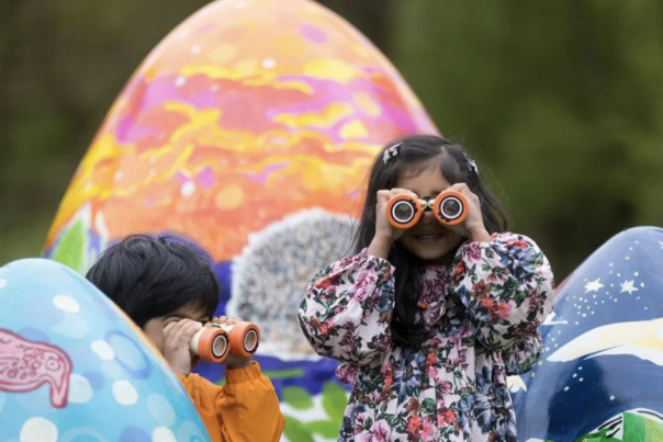 children in puddlesuits looking through binoculars, huge easter eggs in the background