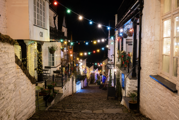 A charming cobblestone street at night, lined with cosy houses adorned with glowing multicoloured string lights, creating a festive, warm atmosphere.