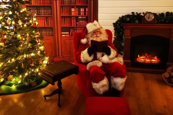 father christmas sitting in an armchair reading a book next to christmas tree