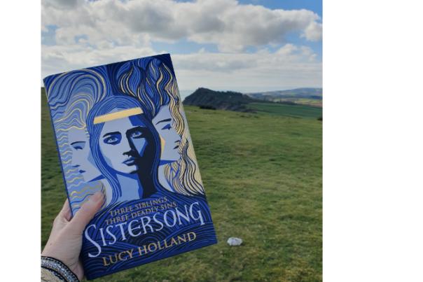 copy of sistersong being held up against backdrop of sidmouth