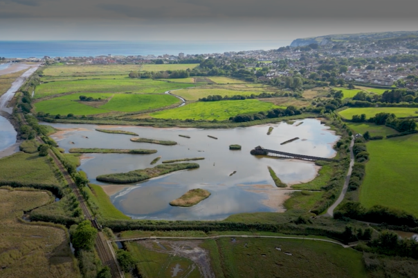 Aerial view of a scenic wetland area with ponds, surrounded by vibrant green fields and distant hills. A tranquil landscape under a clear sky.