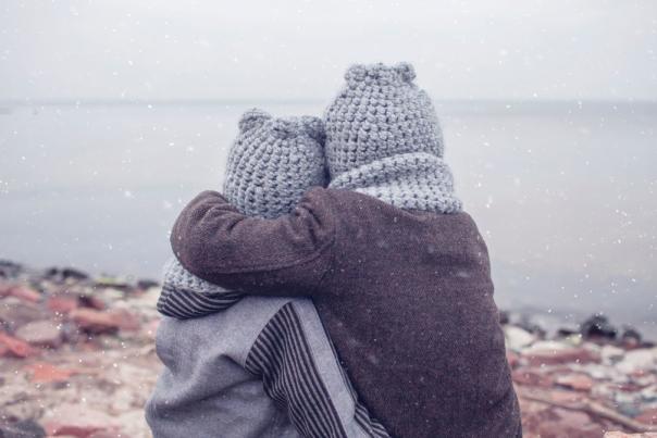 two children in hats having a hug on a wintery beach