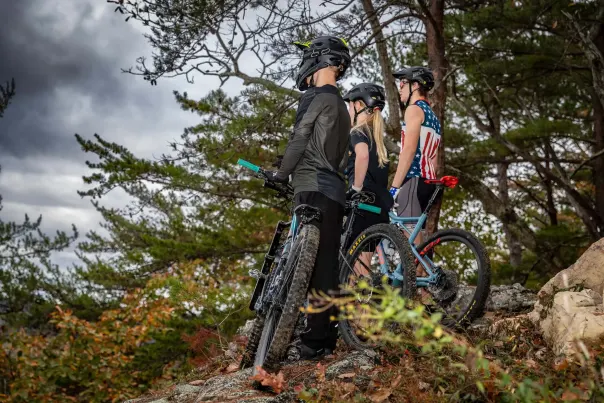 Three young mountain bikers stare out over the view of an overlook during a cloudy day at Double Oak Park. They each are standing next to their mountain bikes.