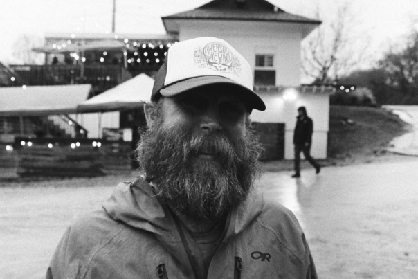 Jason Pruitt, the owner of Oversoul Brewing in Helena, Alabama, smiles in front of the brewery. The photo is black and white.