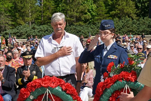 Two people salute and honor a shrine for veterans at the American Village in Montevallo during a Memorial Day ceremony filled with people.