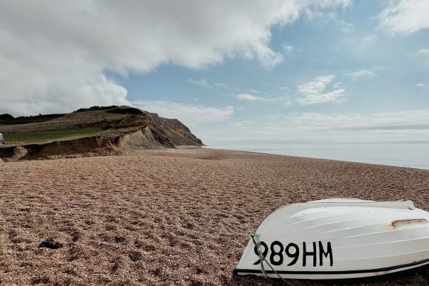 image shows seatown beach looking east, with a white upturned boat in the foreground