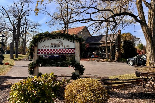 A wooden sign advertising "The Morgan House" in Dublin, Ohio. The sign features a festive design with greenery and a checkered pattern. The Morgan House building, with its red roof and stone facade, is visible in the background.