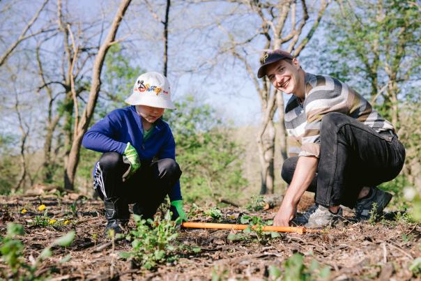 2 individuals crouching on a hill, planting seedlings into the ground.