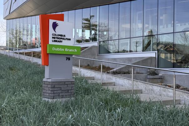 Modern exterior view of the Columbus Metropolitan Library – Dublin Branch, featuring glass walls and the vibrant green and orange library sign at 75 N. High Street.