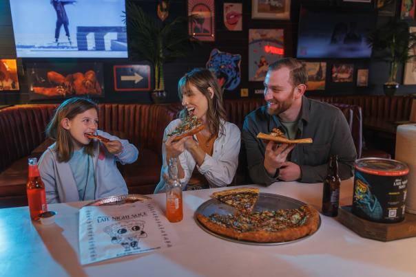 A smiling family enjoys pizza and sodas together at a booth inside Mikey’s Late Night Slice in Dublin, Ohio.