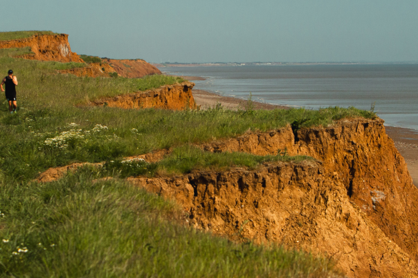 Two people running on the coastal path with the beach and sea to their right.