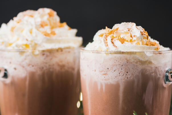 A close up of two hot chocolates in glass mugs, topped with lashings of cream.
