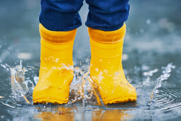 A child wearing yellow wellies jumping in a puddle
