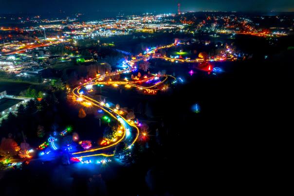 An aerial nighttime view of a brightly lit, winding pathway surrounded by colorful lights, set against the backdrop of a glowing cityscape.