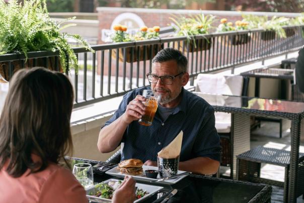 A man and woman are dining outside at J.R. Neighbors. The man is drinking a glass of beer while looking at the woman sitting across from him