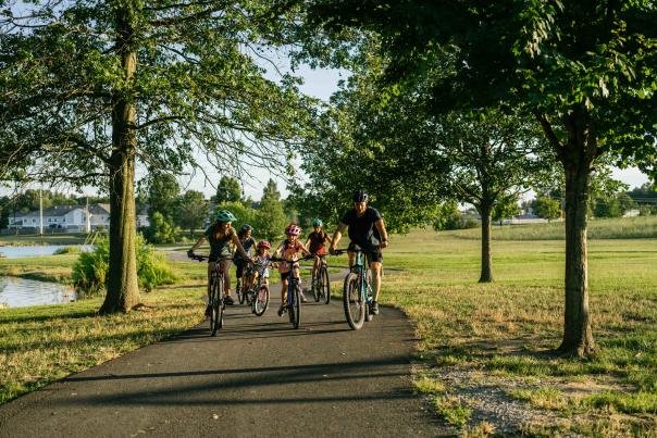 A group of people, including children, riding bicycles together on a paved path in a scenic park during a sunny day.